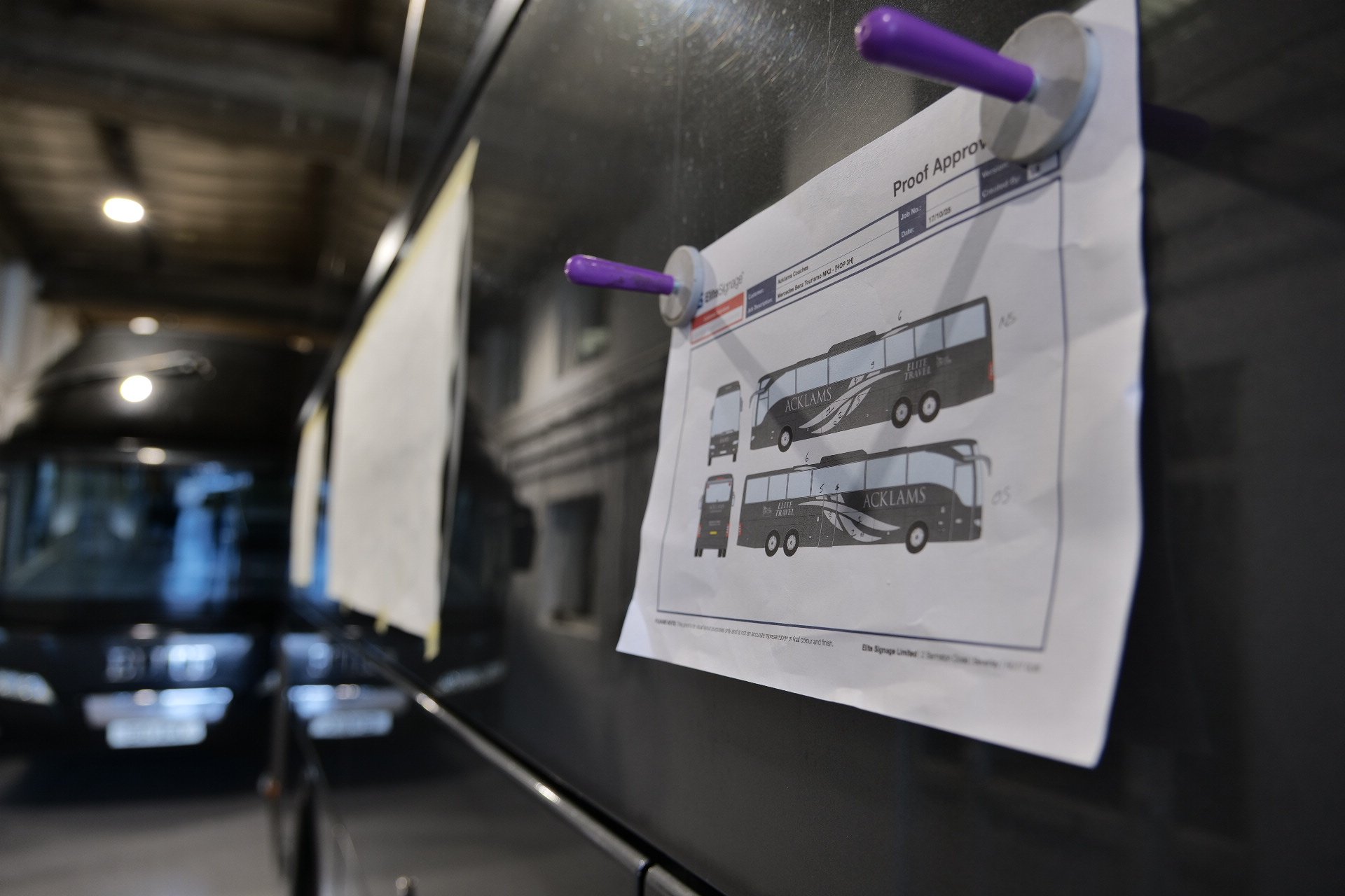 Design plans for a bus, pinned to a black wall with purple thumbtacks, showing side and back views labeled 'ACKLAMS' with decorative graphics.