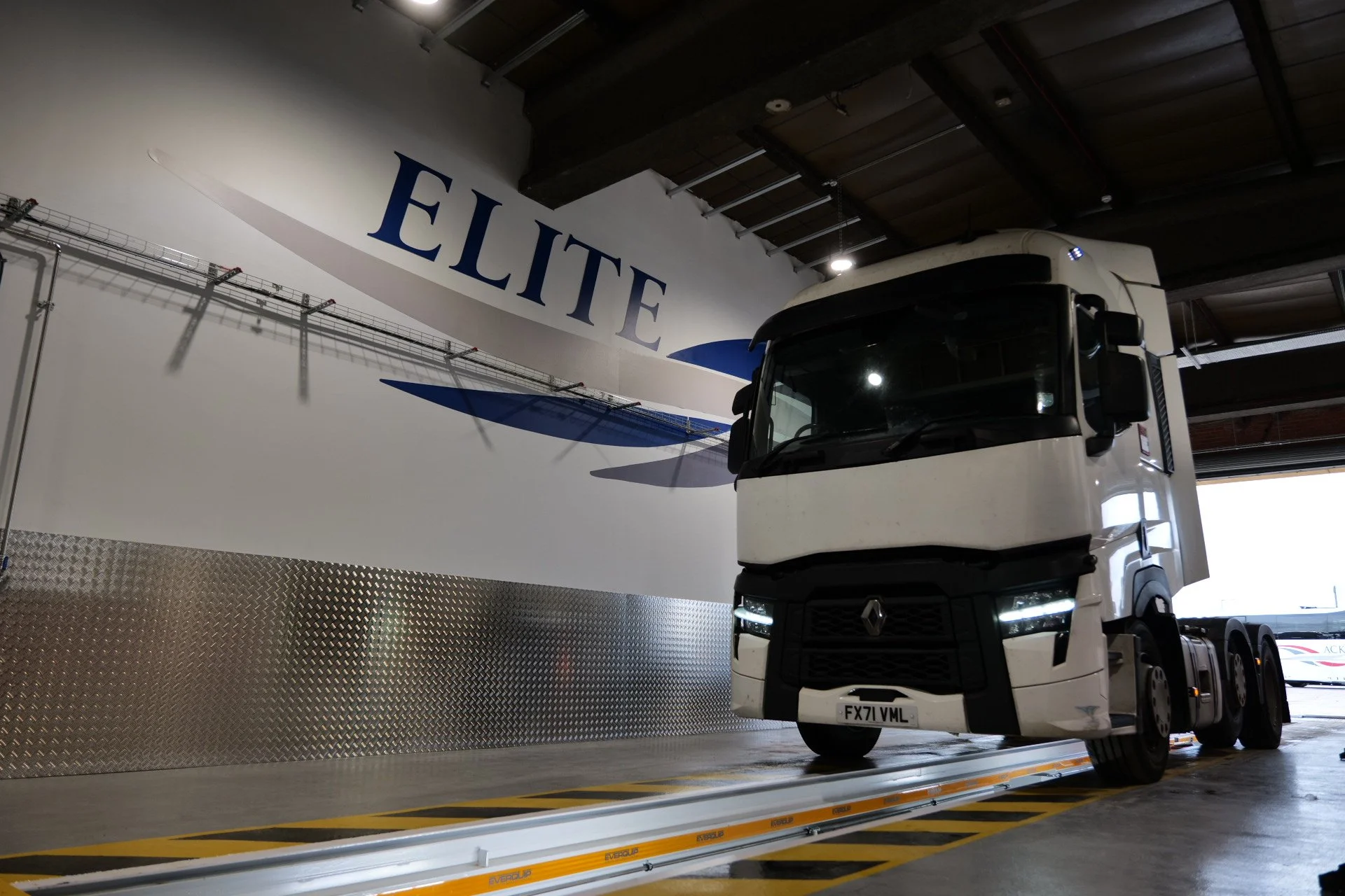 A white Renault truck inside a garage with a large "ELITE" sign and a boat in the background.