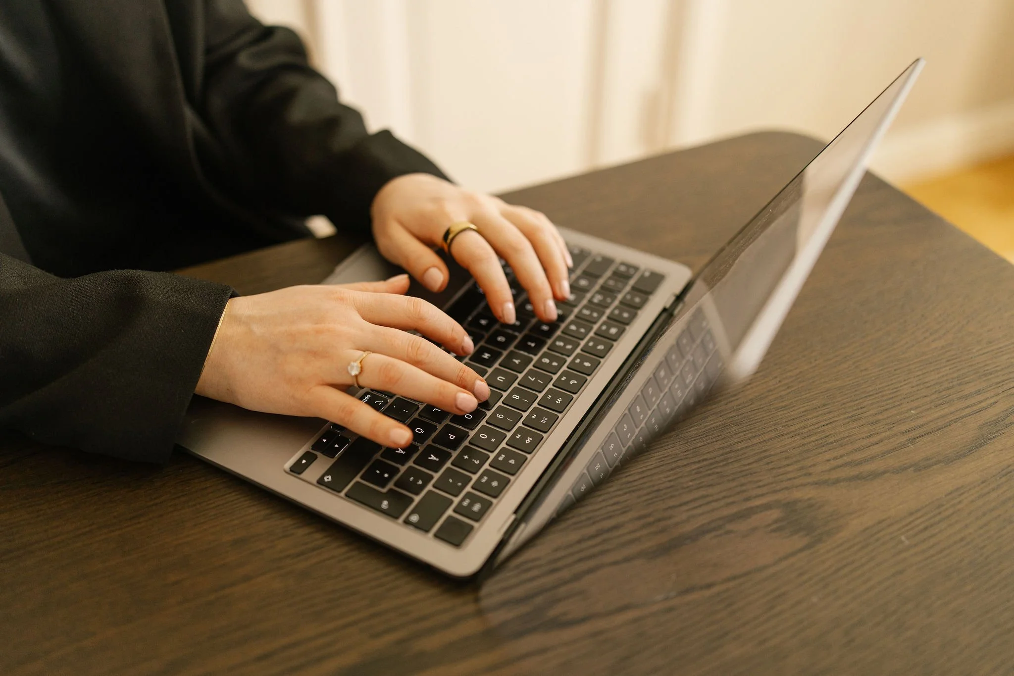 Person wearing rings typing on a laptop keyboard on a wooden table.