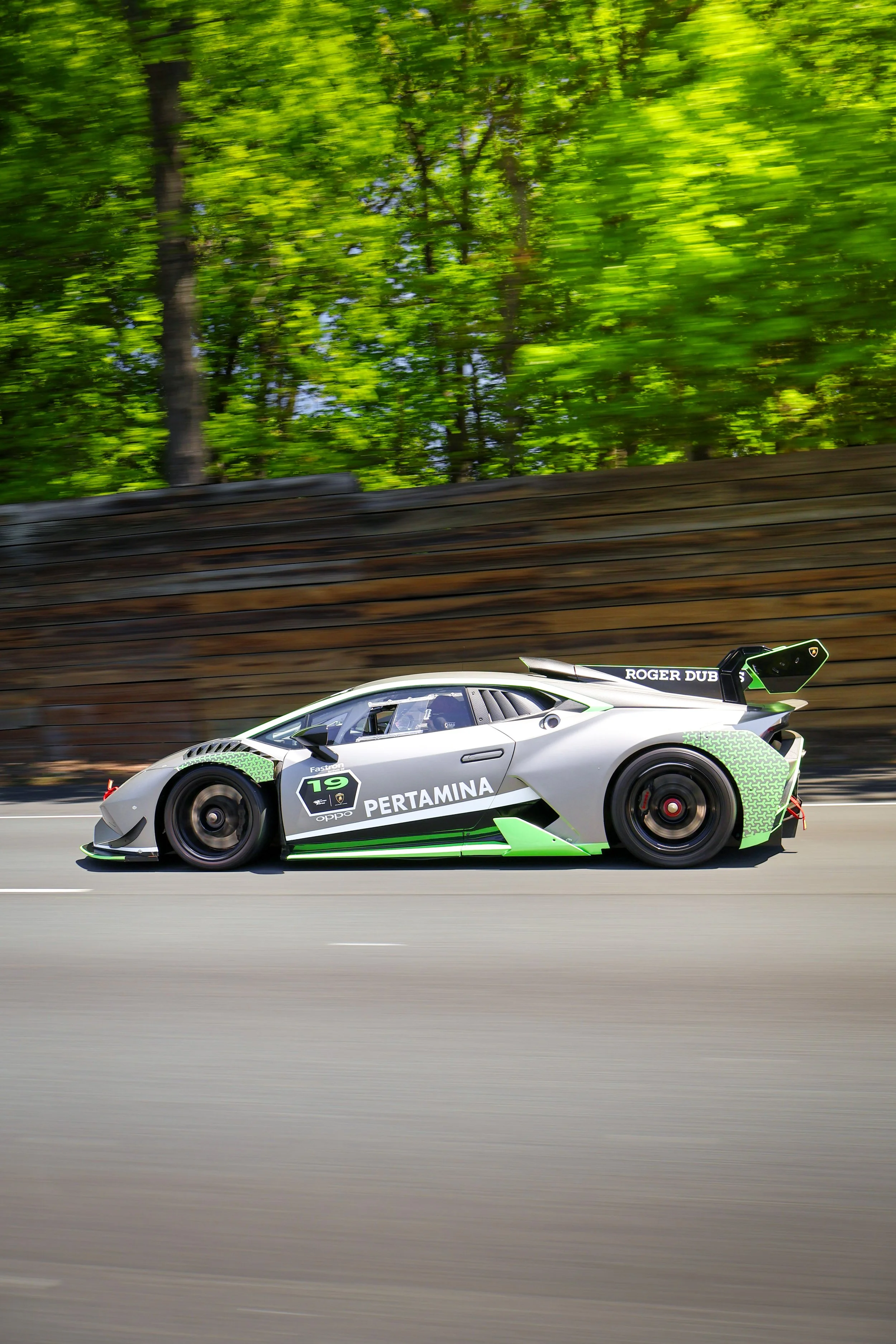 A race car speeding on a track with a blurred green trees background.
