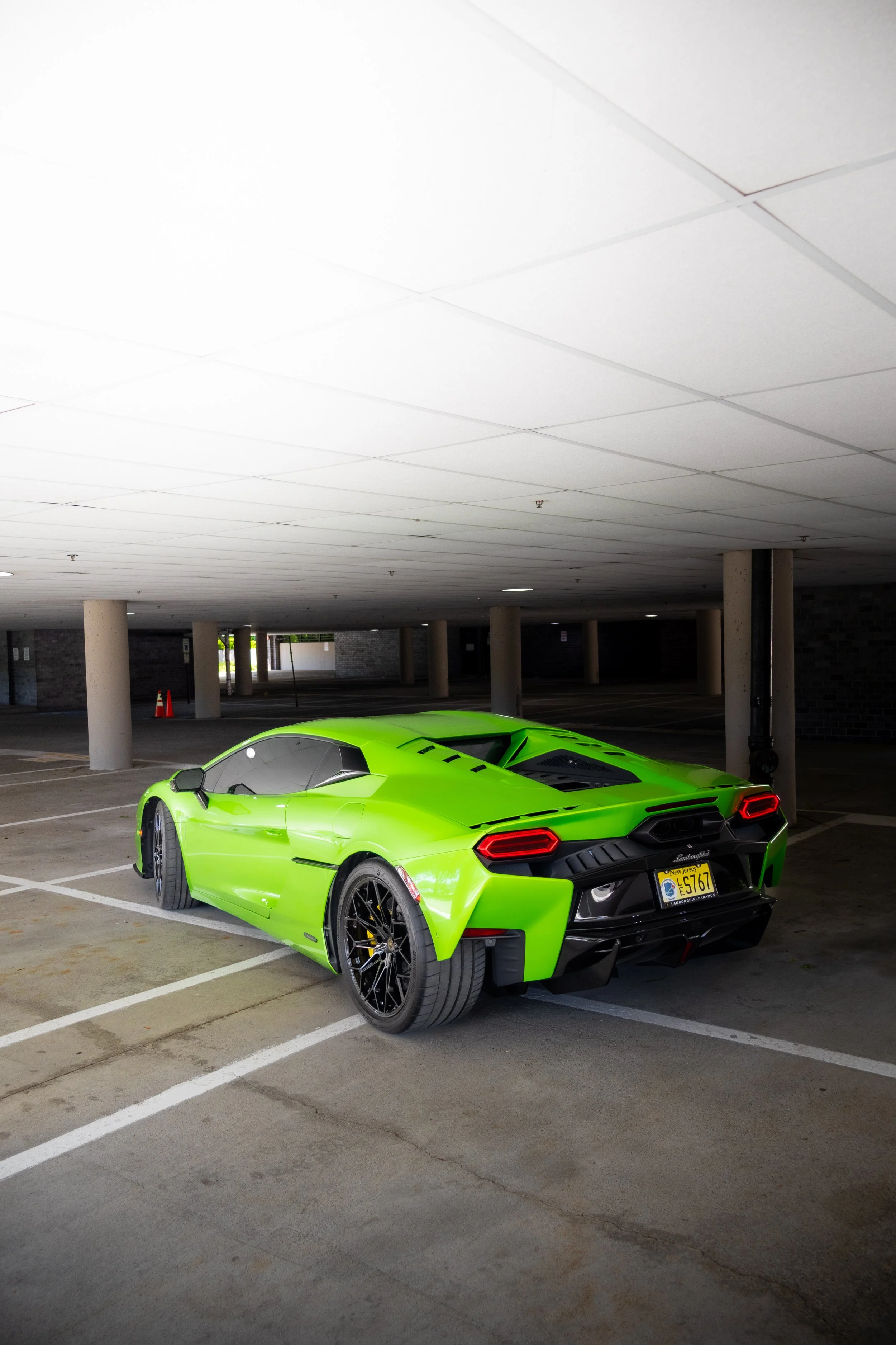 Bright green Lamborghini sports car parked in an outdoor parking lot under a covered structure, with a yellow license plate and black rims.