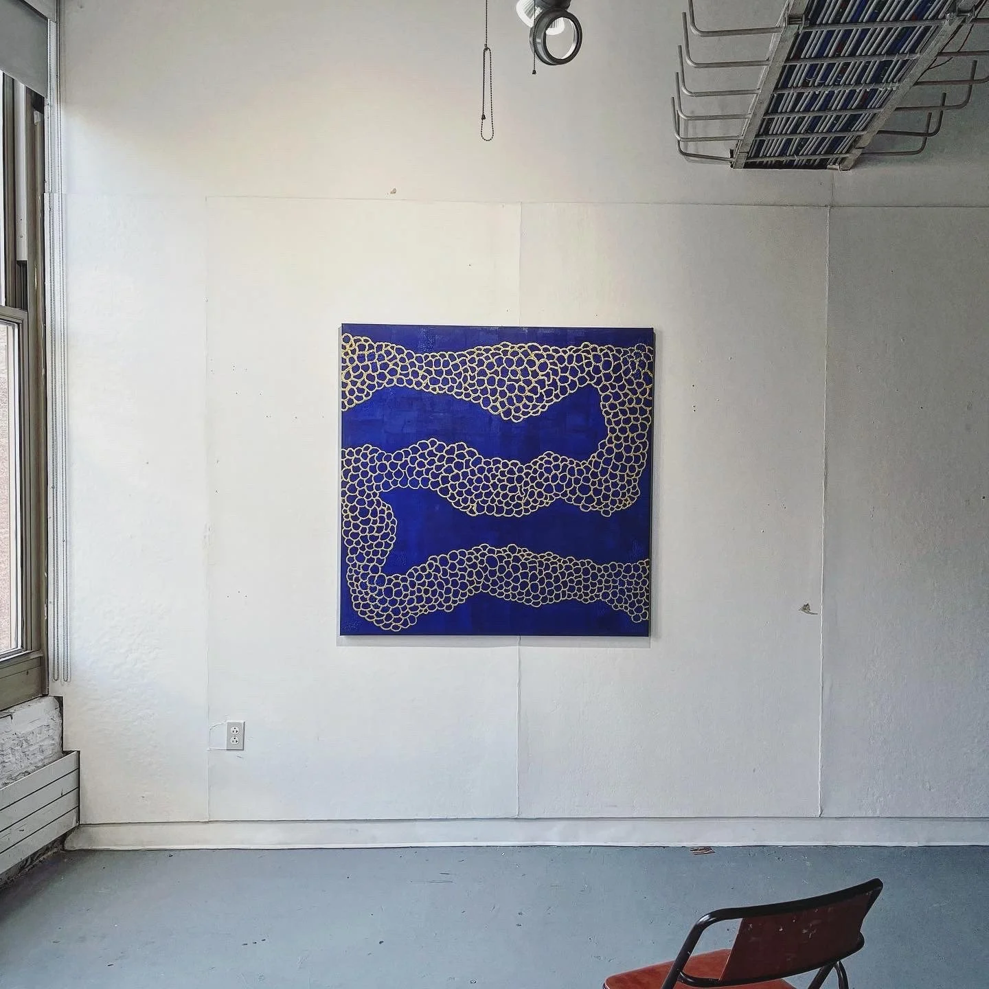 An abstract painting with blue background and white circular patterns hangs on a white wall in an art gallery or studio.