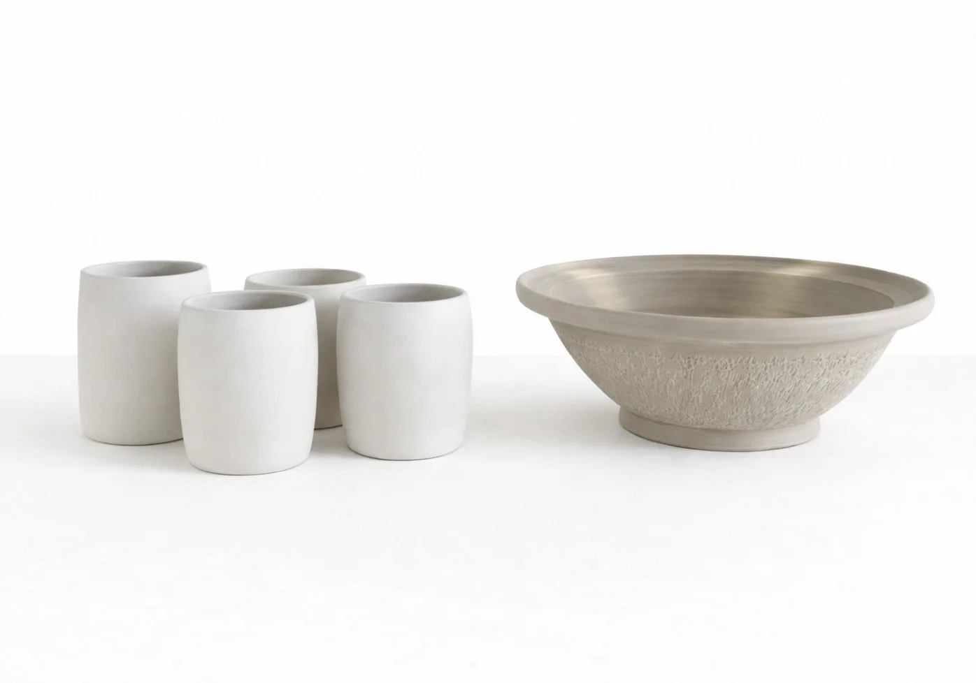 Set of four white ceramic drinking cups and one large beige ceramic bowl on a white background.