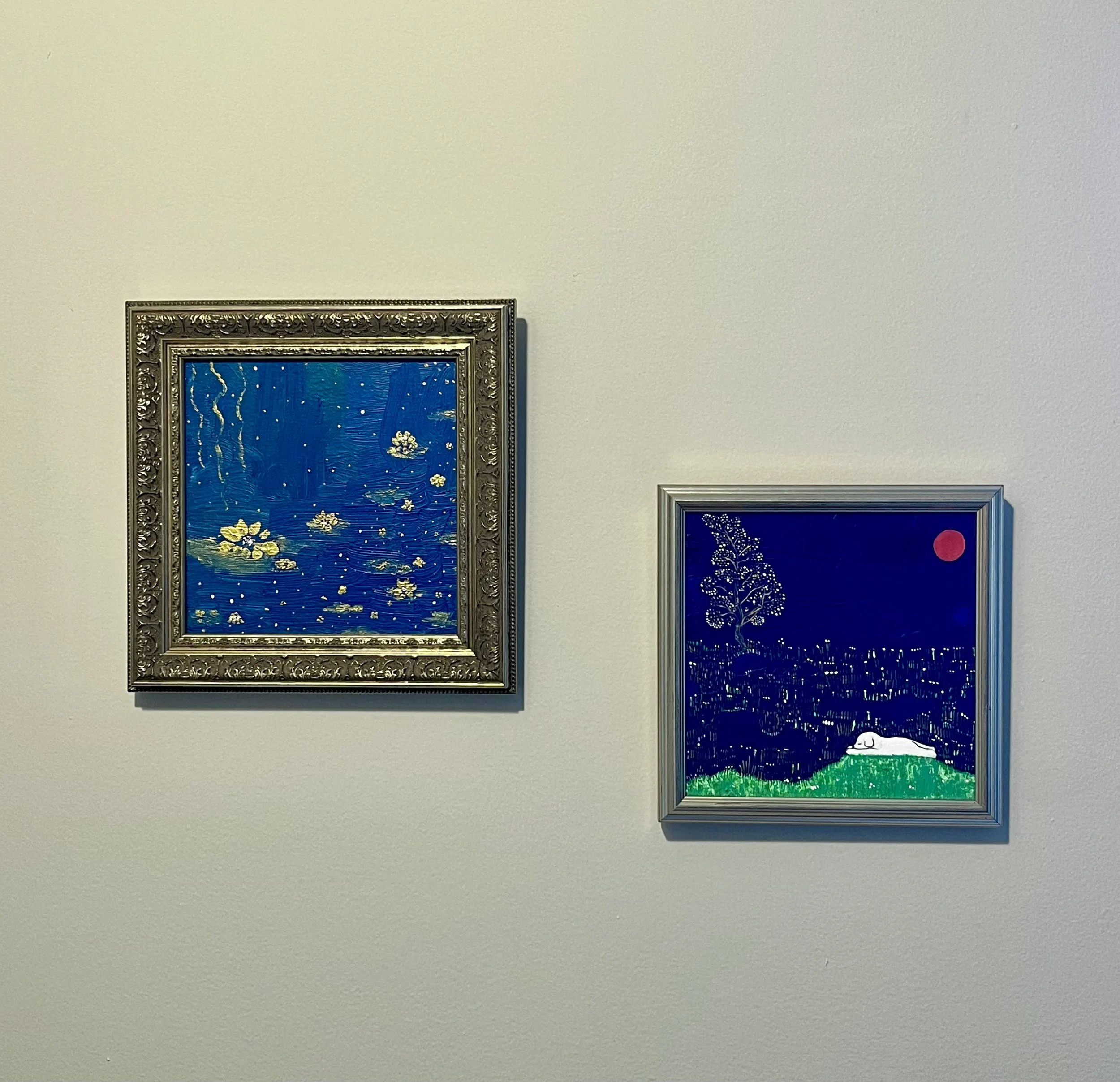 Two framed artworks on a white wall, one depicting Van Gogh's Starry Night with a decorative silver frame, and the other a stylized night scene with a white sleeping cat, a tree, and a red moon with a silver frame.
