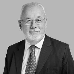 Black-and-white photo of an older man with white hair and a beard, wearing glasses, a suit, and a patterned tie.