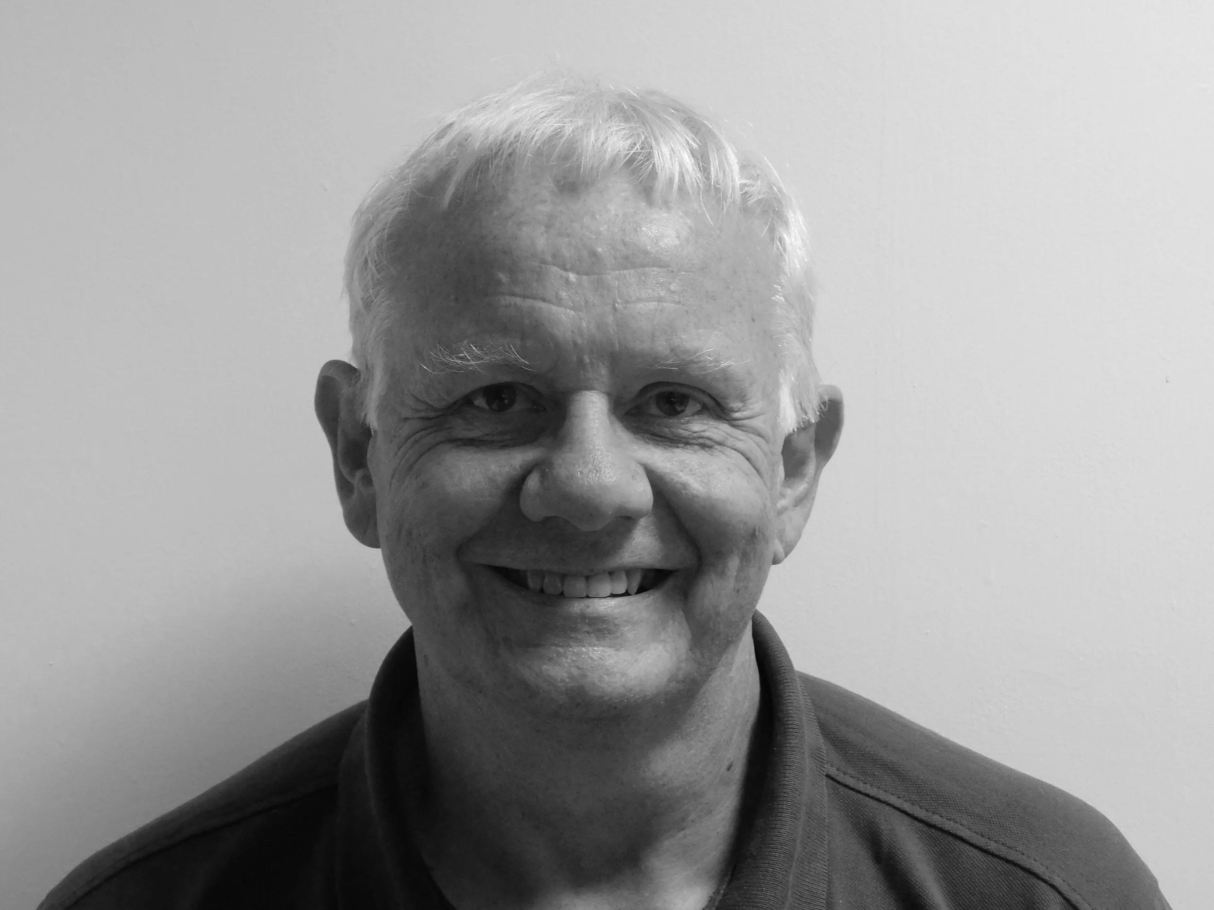 Black and white portrait of smiling middle-aged man with short light-colored hair, wearing a collared shirt against plain background.