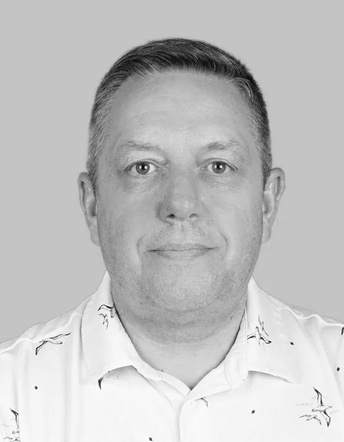 Black and white headshot of a man with short hair, wearing a collared shirt with a bird pattern, against a plain background.