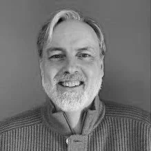 A smiling middle-aged man with gray hair and a beard, wearing a sweater.