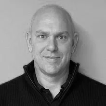 Black and white headshot of a middle-aged man with a slight smile, wearing a dark zip-up sweater over a collared shirt.