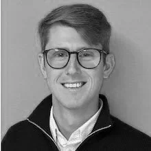 Young man with glasses smiling, dressed in a collared shirt and jacket