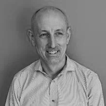 Black and white portrait of a smiling middle-aged man with short hair, wearing a collared shirt, against a plain background.