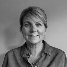 Black and white portrait of a woman with short hair, wearing a collared shirt and earrings, smiling at the camera.