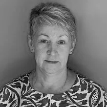 Black and white photo of a woman with short hair, wearing a patterned top, facing the camera with a neutral expression.