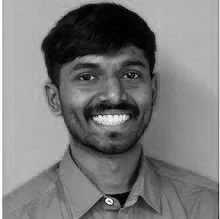 A smiling young man with dark hair and a mustache, wearing a collared shirt, in black and white.