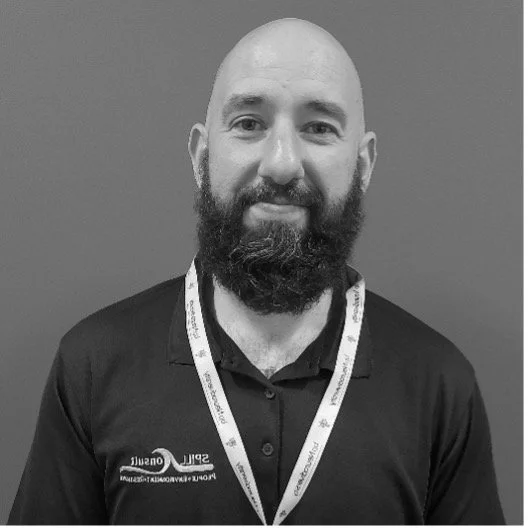 A man with a beard and bald head smiling, wearing a polo shirt and a lanyard.