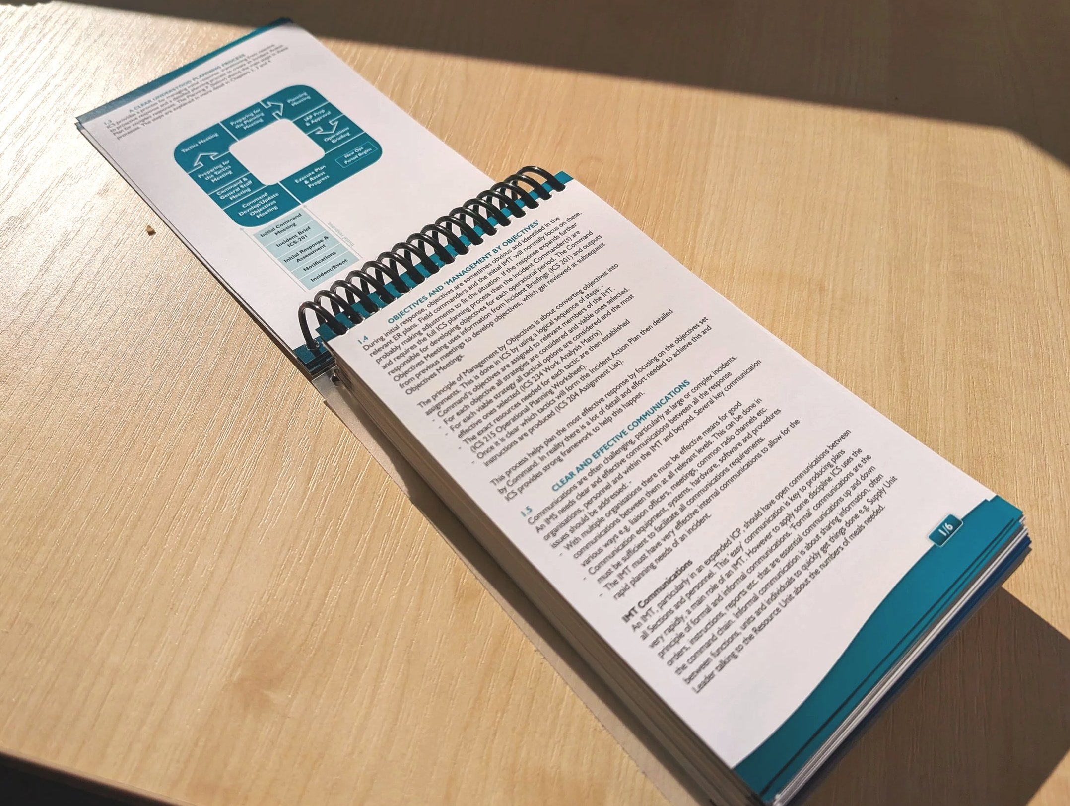 A spiral-bound booklet or manual on a light wooden surface, with a diagram of a process or flowchart at the top of the page and detailed text below.