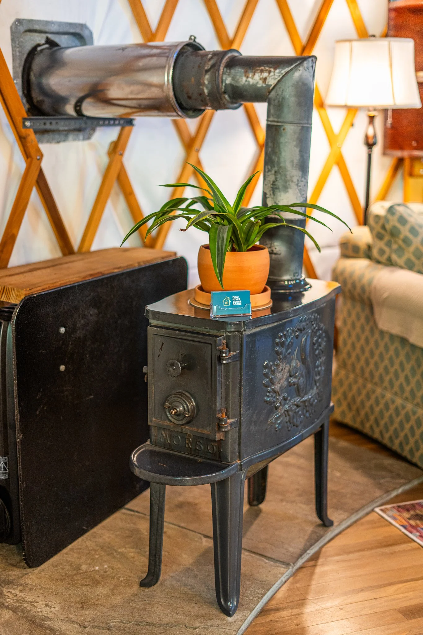 Black wood stove with a potted plant on top, in the cozy yurt at New River Nooks in New River Gorge WV.