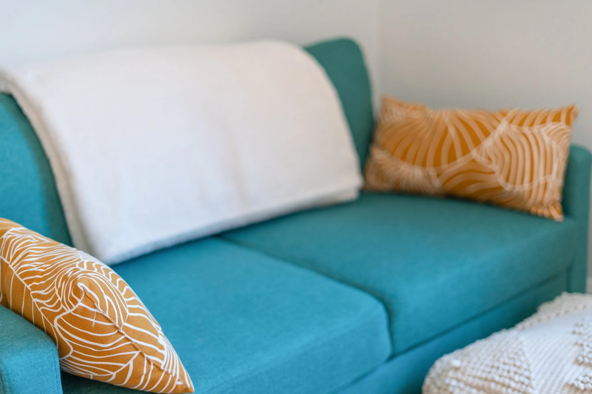 Teal sofa with yellow pillow and white throw blanket in Cloud 9 Loft Apartment in New River Gorge WV.
