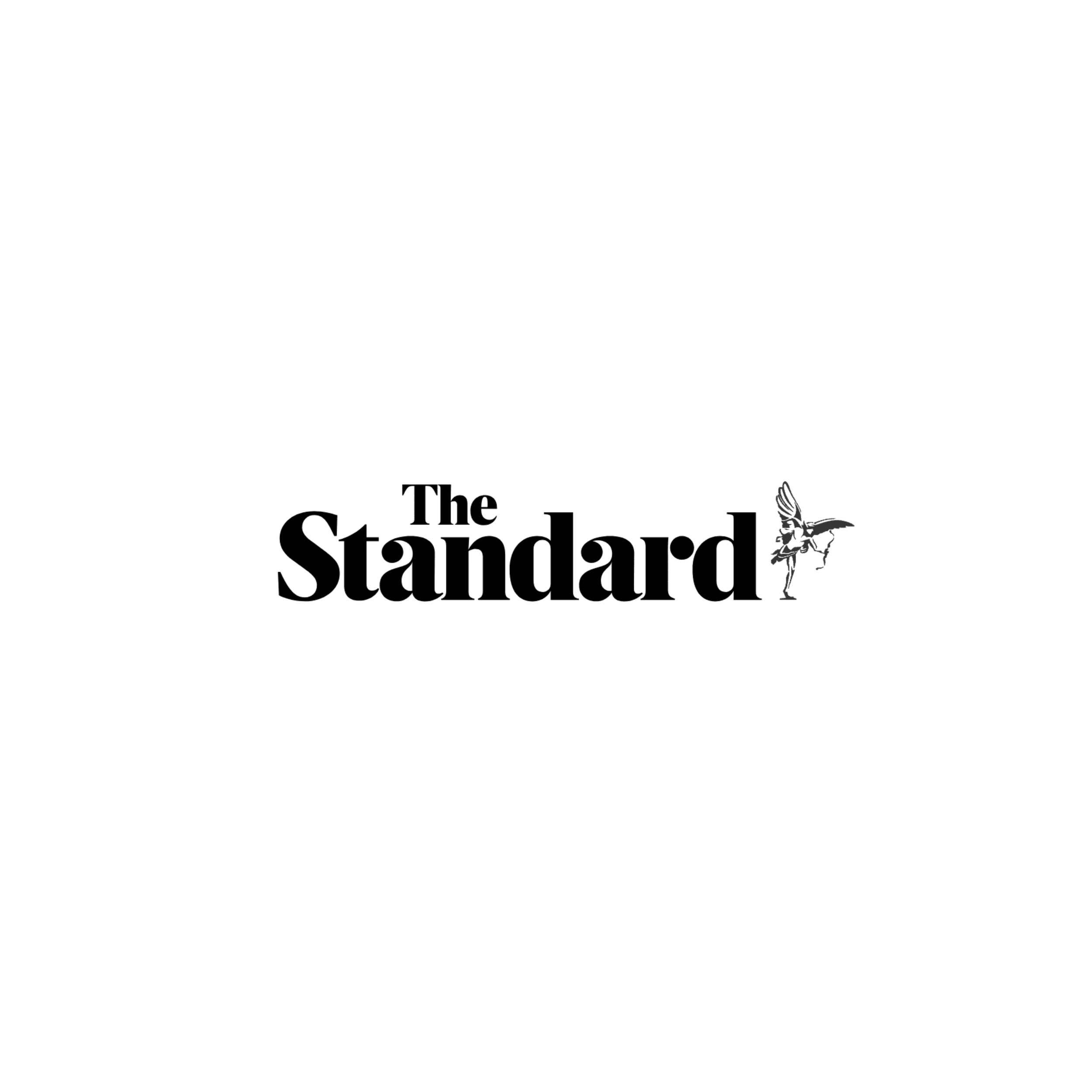 A person dressed in dark clothing, standing on a stage with their right leg raised and arms extended outward, performing a dance or theatrical act. The background is a dark space with a curtain to the right, and there are scattered lights on the floor.