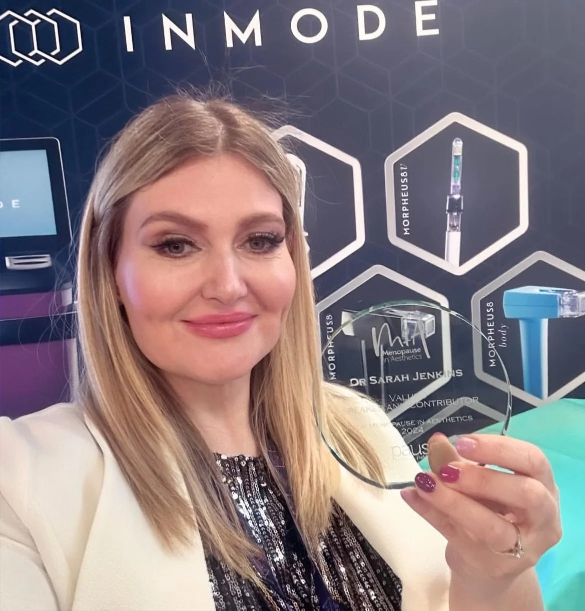 Woman smiling and holding an award at a conference with a backdrop displaying medical and aesthetic products.