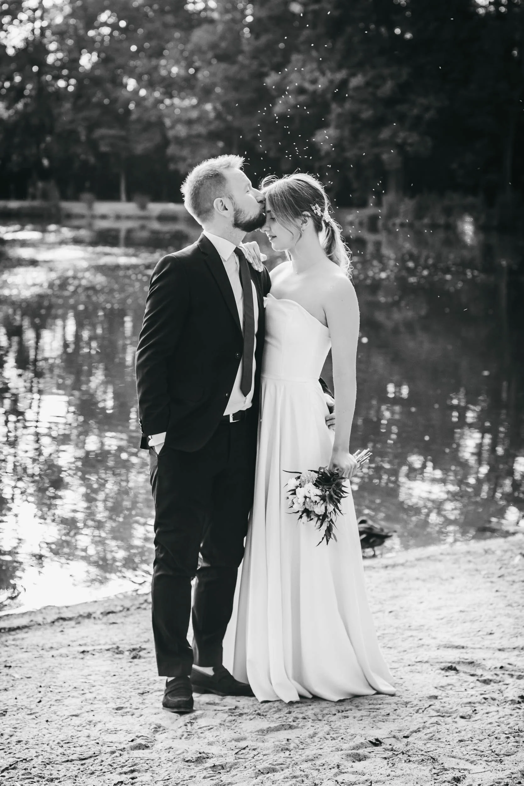 Black and white wedding portrait of the bride and groom kissing by the lake