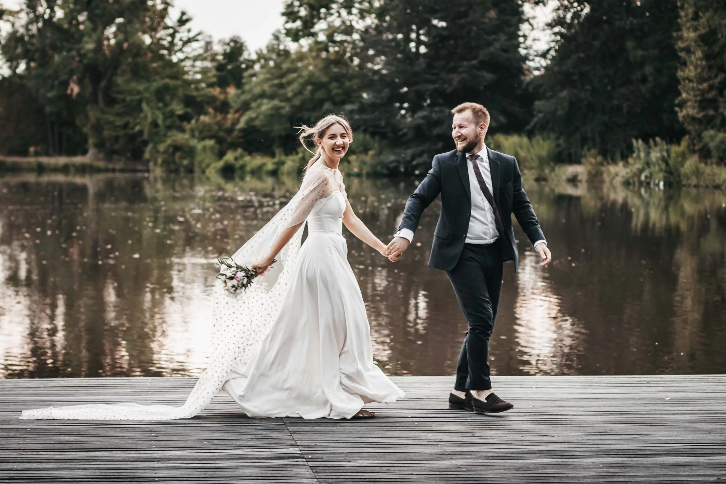 Bride and groom walking hand in hand on a dock by the lake