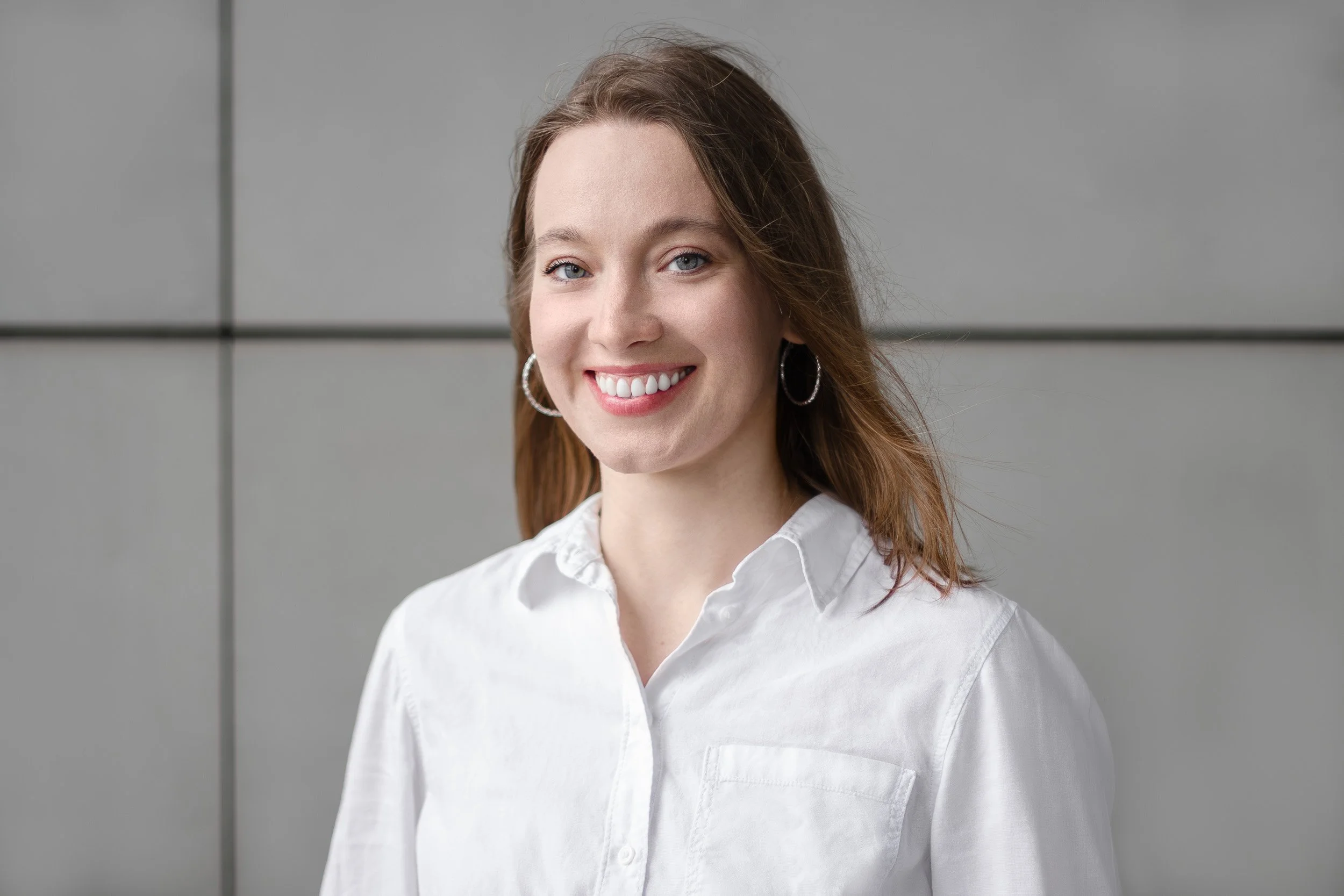 Woman in a white shirt smiling in front of a gray wall.