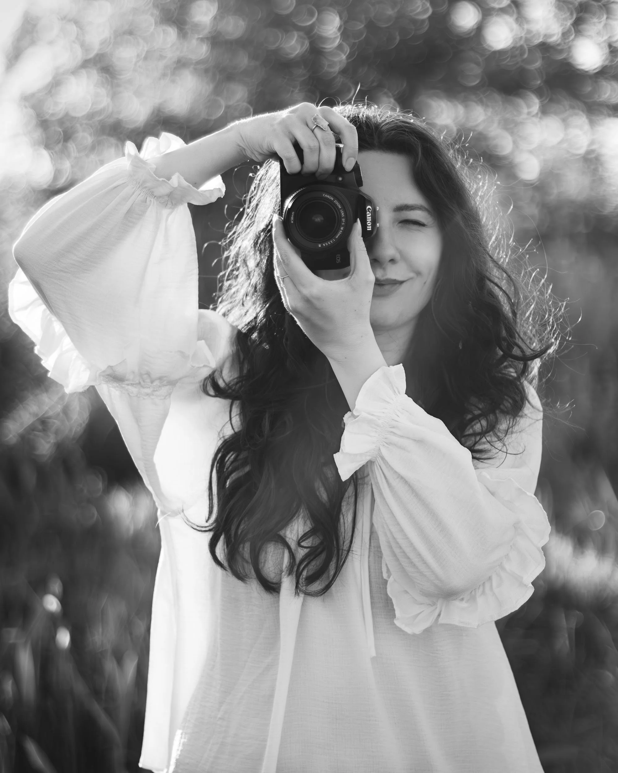 Black and white self portrait of a photographer Aleksandra holding a camera outdoors.