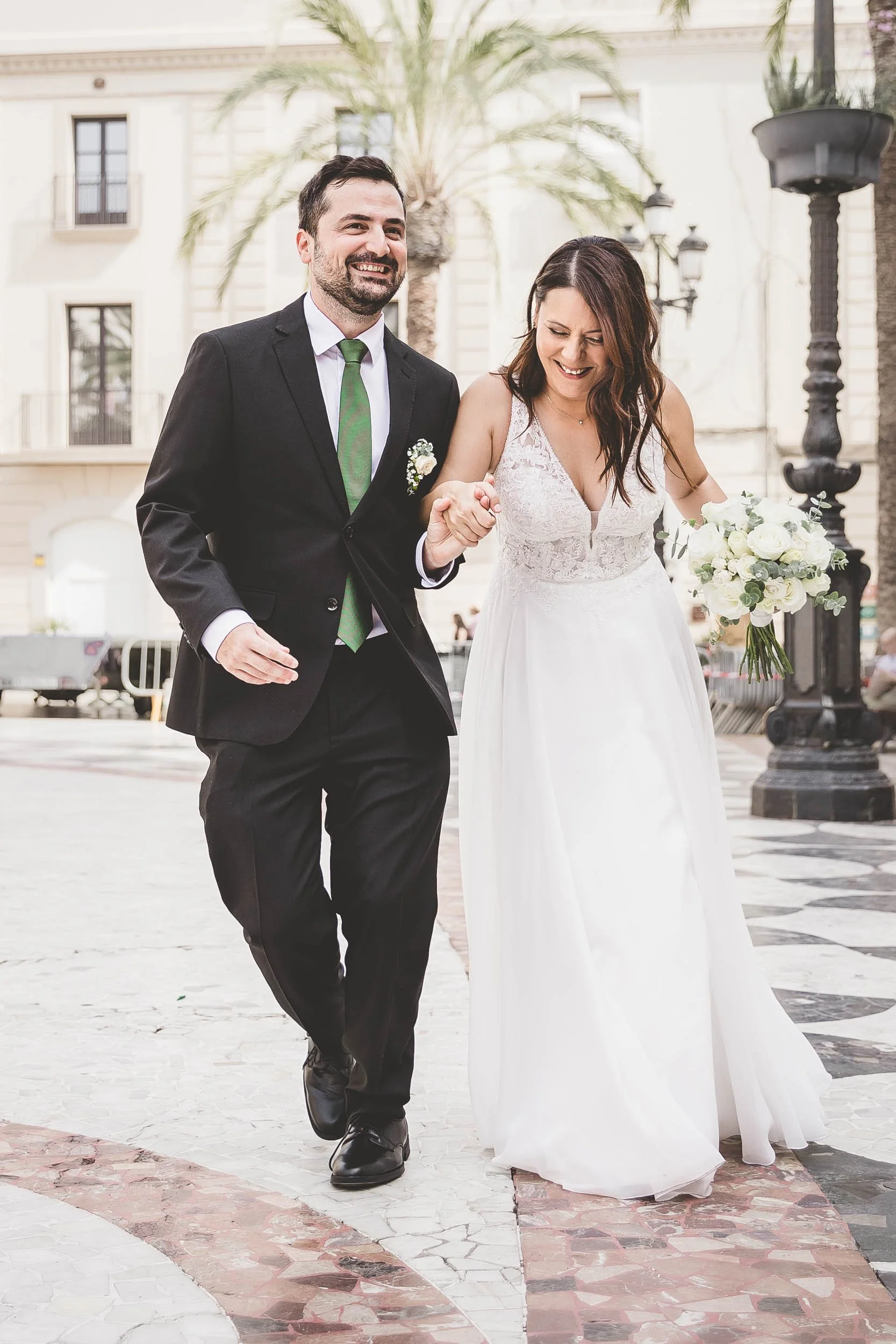 Bride and groom walking hand in hand outdoors after the ceremony, smiling as the bride holds a white bouquet.
