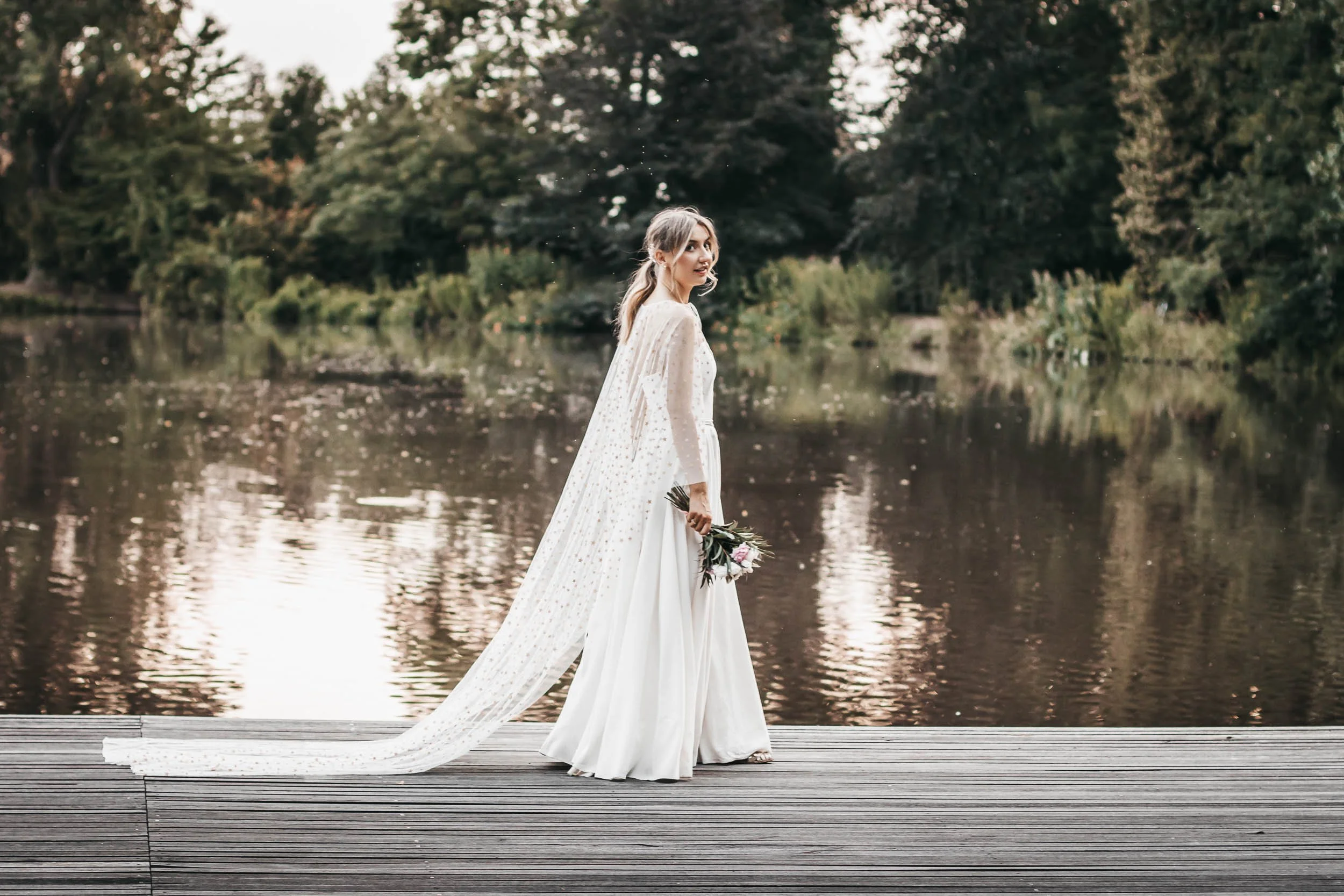 Full-length bridal portrait on a dock by the lake with the veil flowing behind