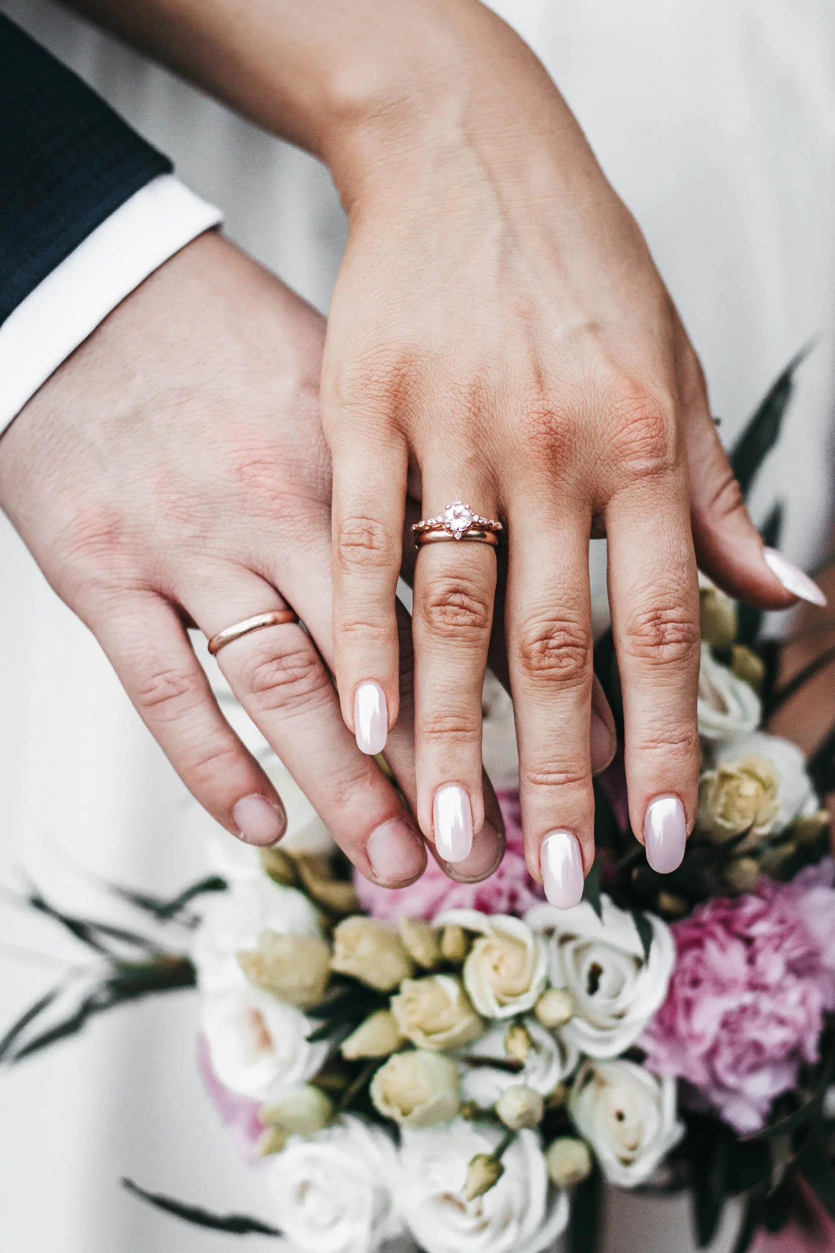 Close-up of the bride and groom's hands with wedding rings resting over the bouquet