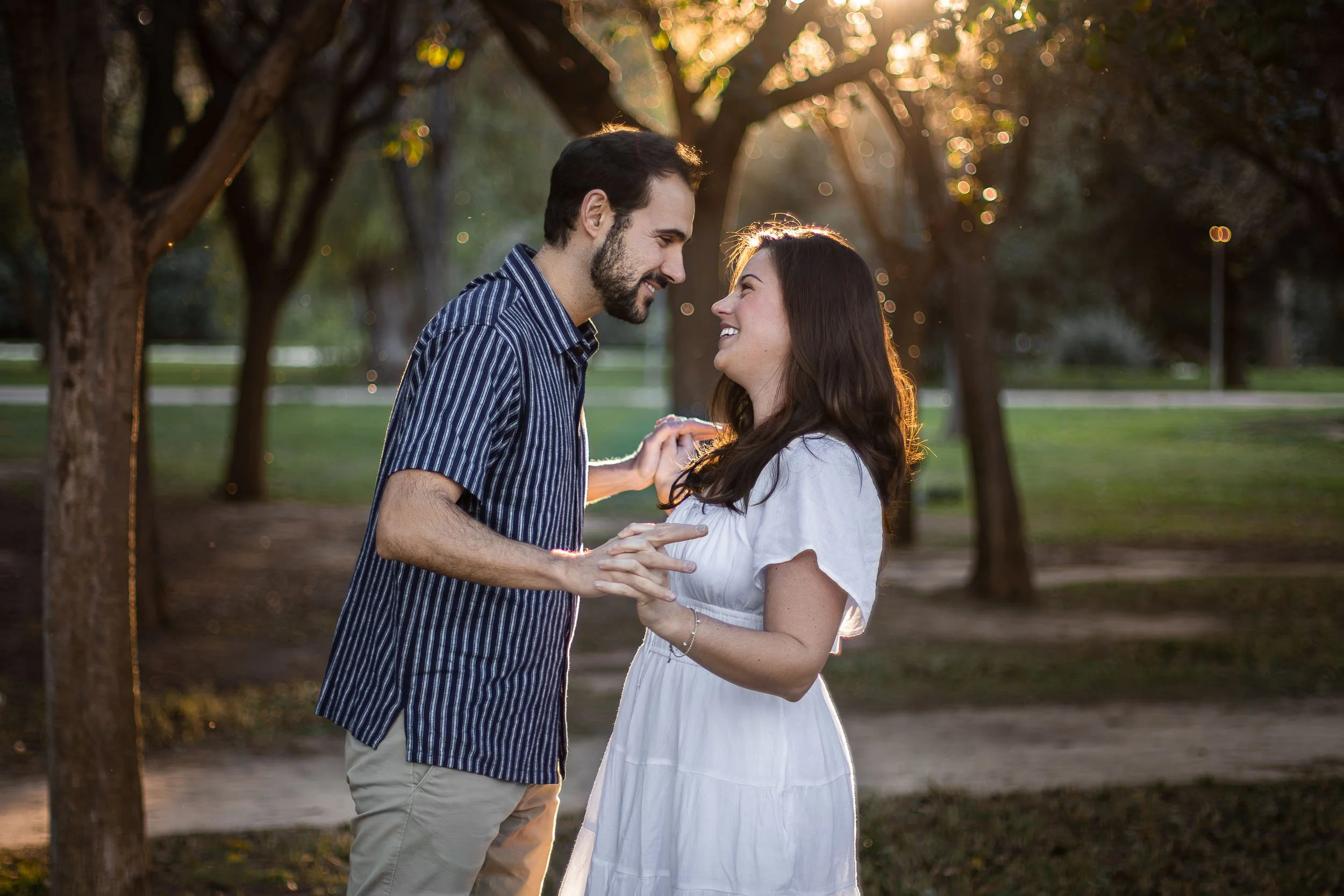 Portrait of a couple holding hands and smiling at each other in a park at sunset