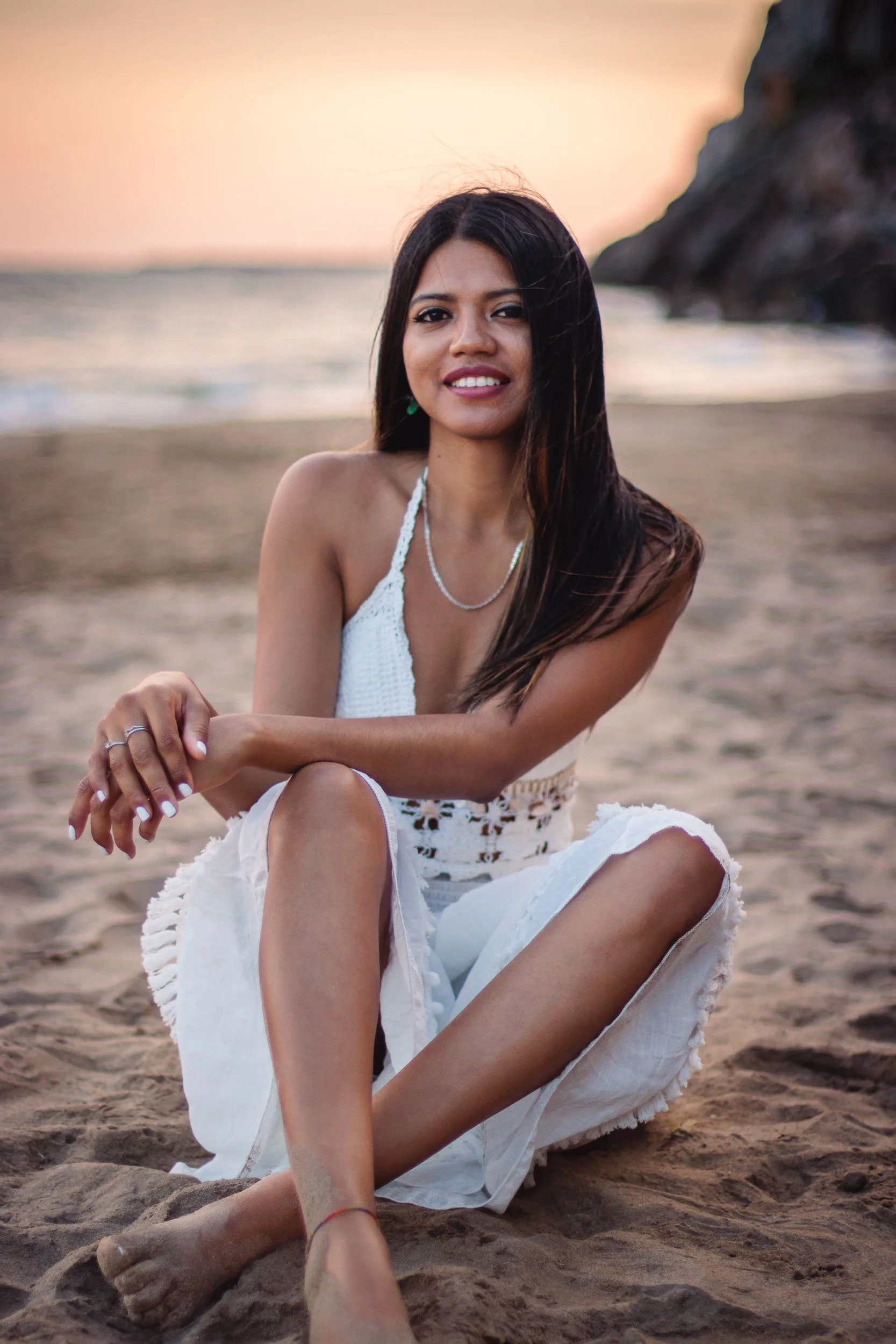 Portrait of a smiling woman seated on the beach in a white dress