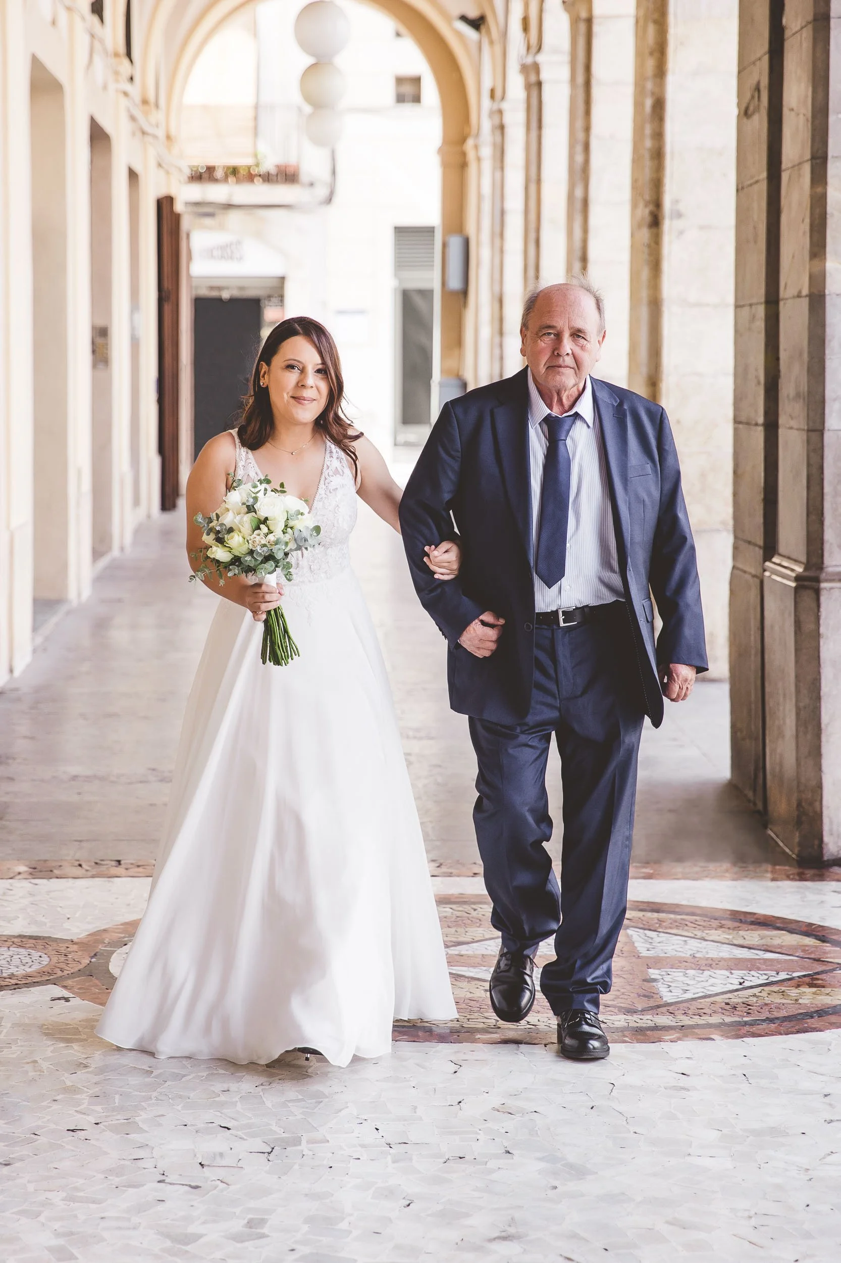 Bride walking with her father through an arcade before the wedding ceremony