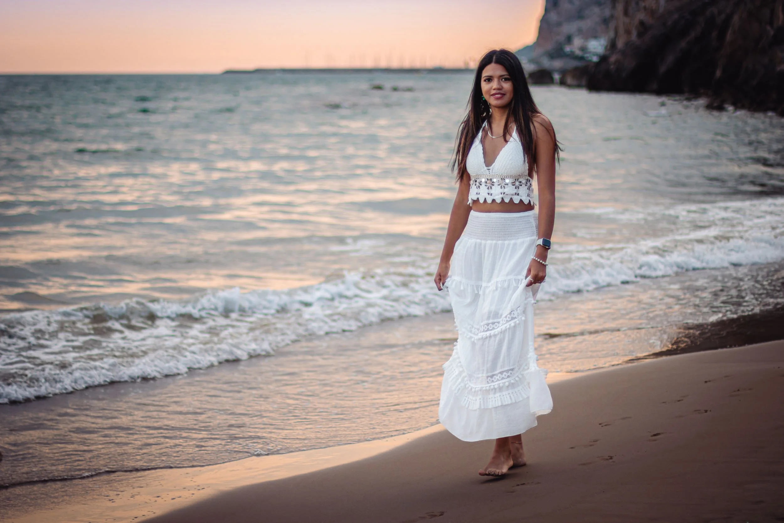 Full-length portrait of a woman walking along the shoreline at sunset