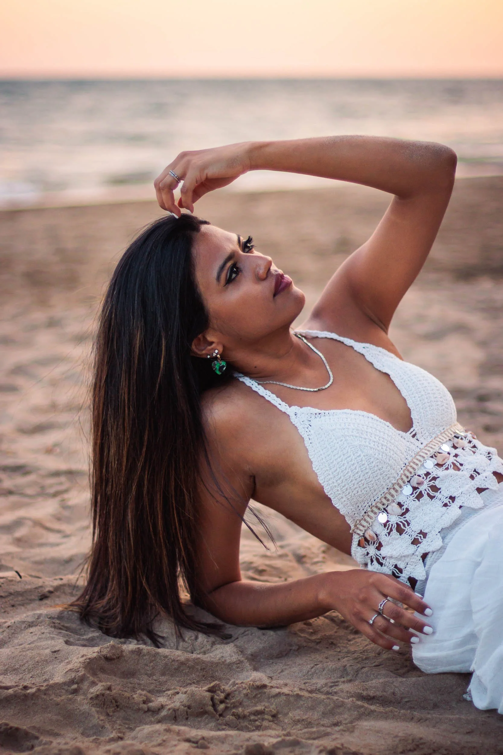 Portrait of a woman reclining on the sand in a white dress at sunset