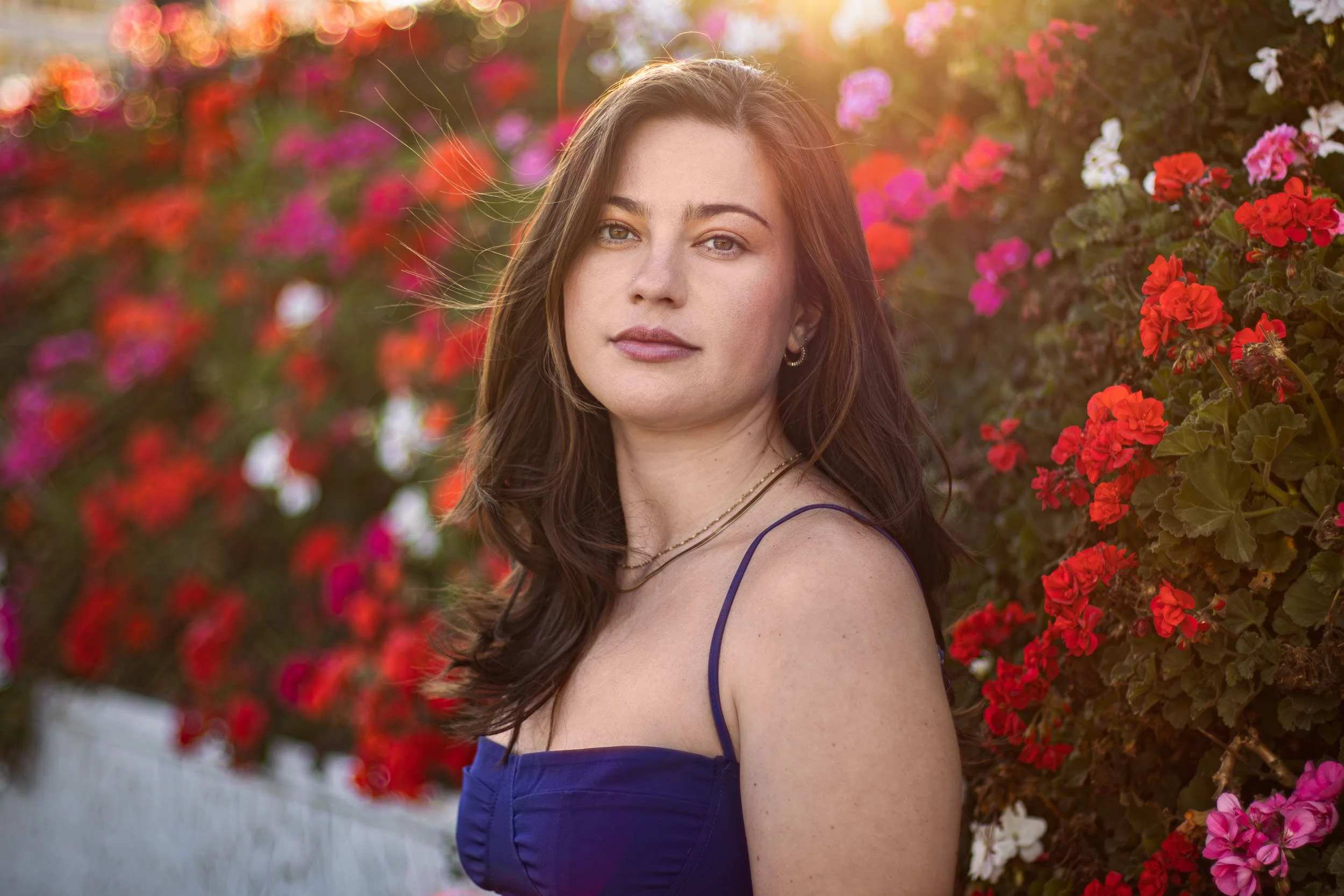 Woman posing outdoors beside bright red and pink flowers.