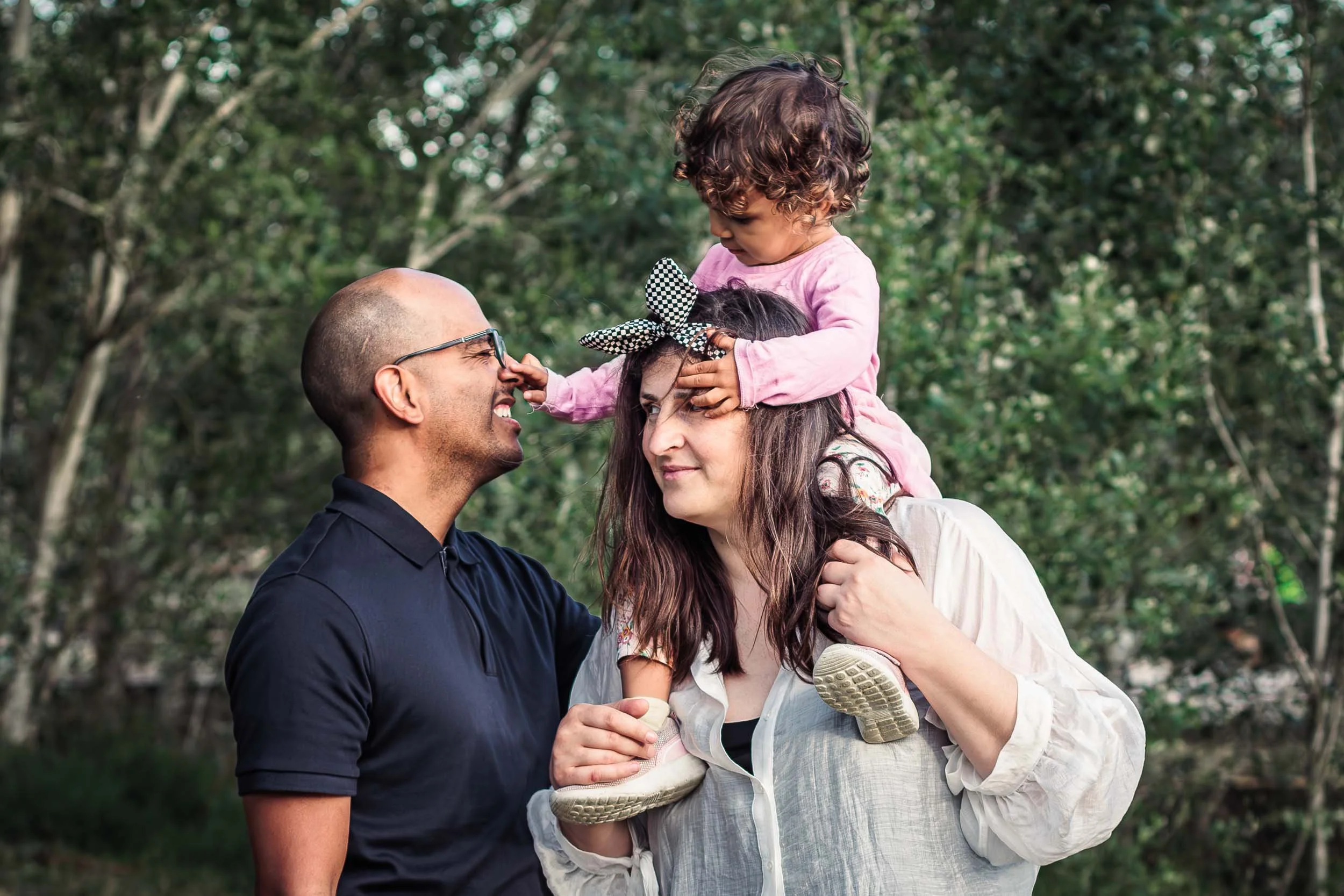Portrait of two parents with their daughter sitting on her mother's shoulders during an outdoor family session