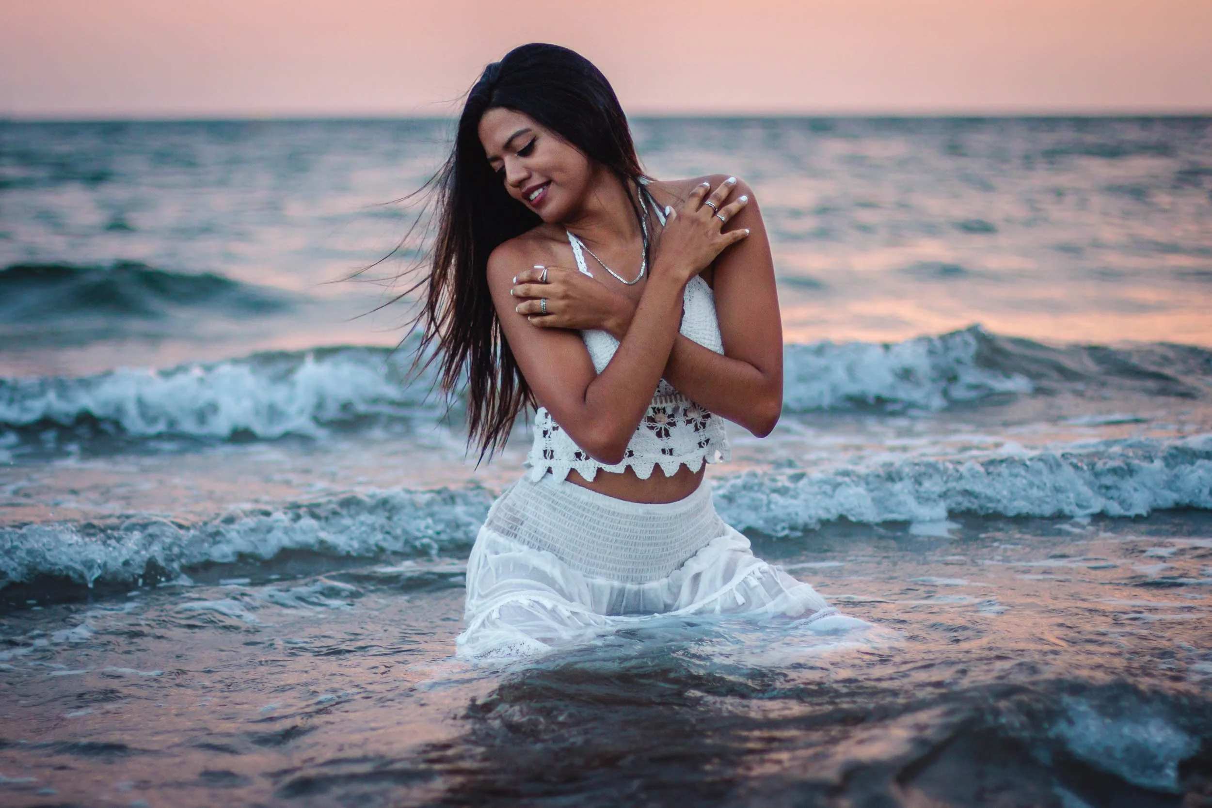Portrait of a woman sitting in shallow water by the sea at sunset