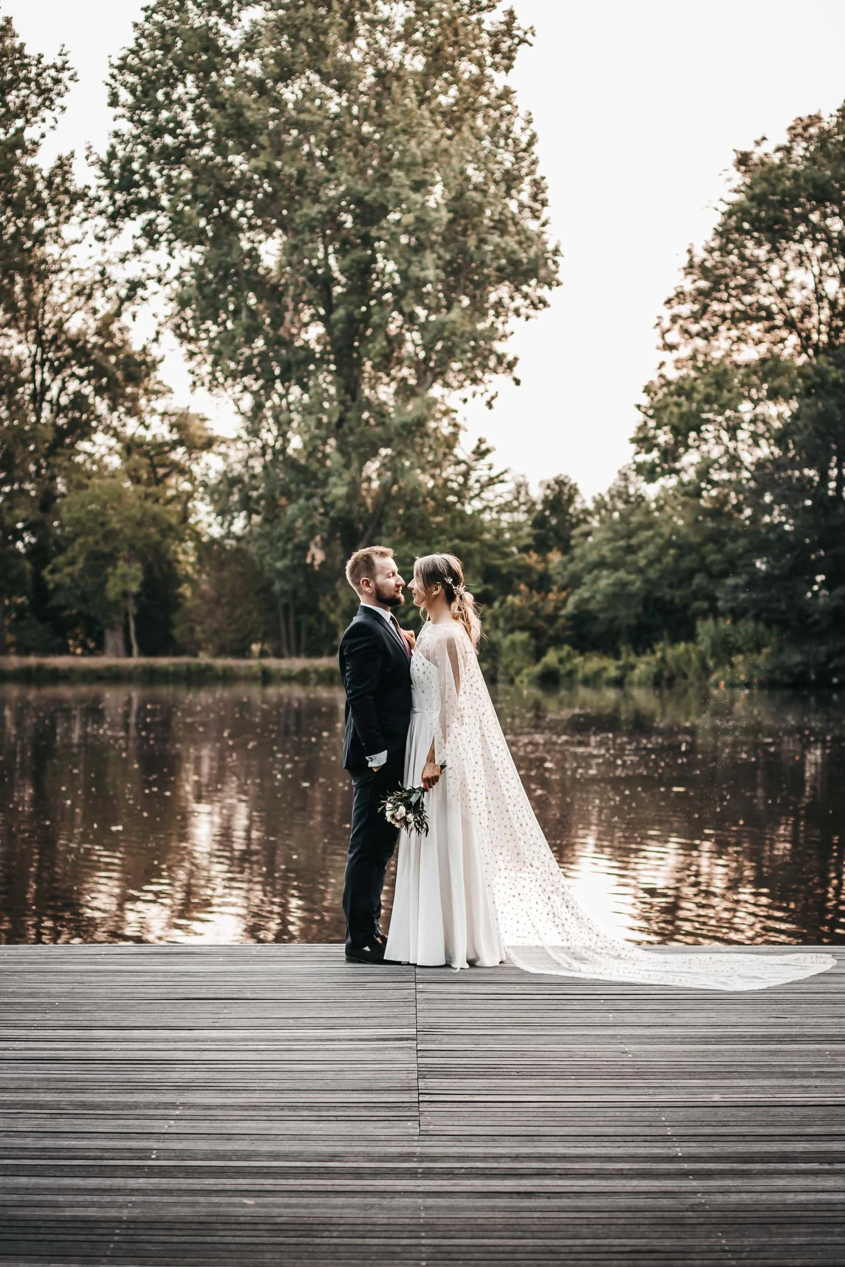 Bride and groom standing together on a dock by the lake
