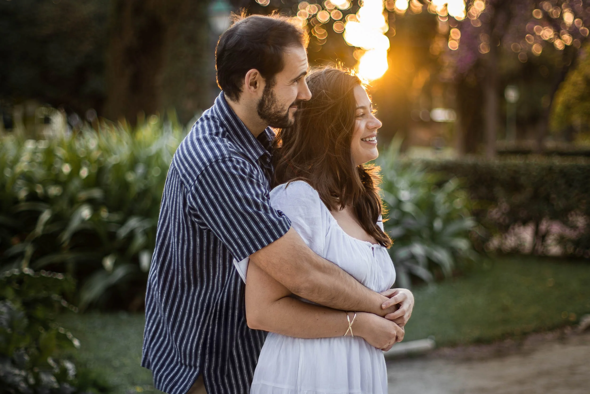 Side portrait of a couple embracing in soft golden-hour light in a park