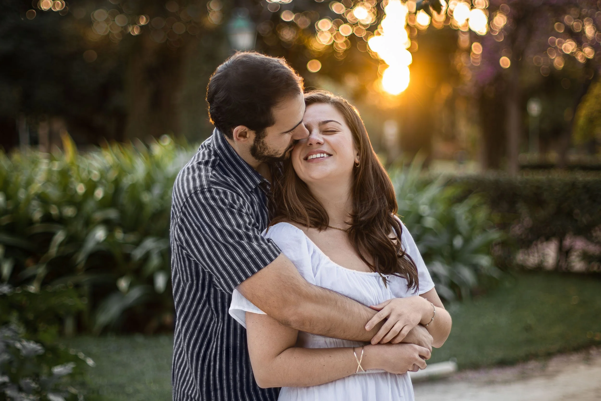 Portrait of a man kissing his partner on the cheek while she laughs in golden-hour light