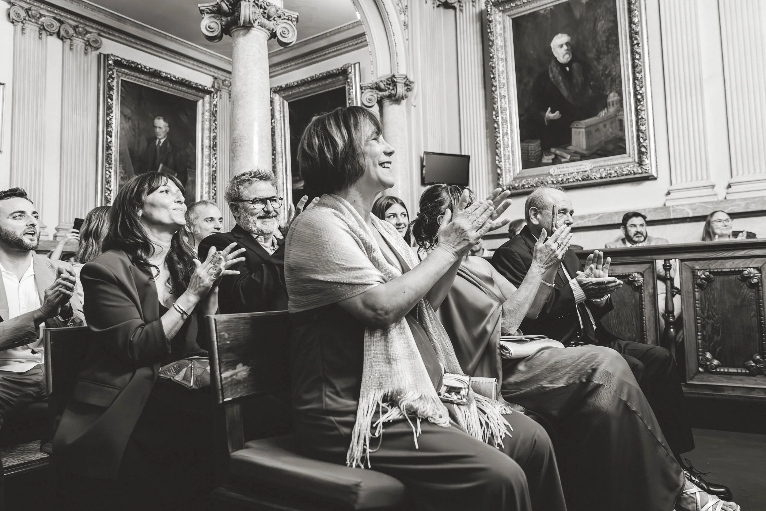 Wedding guests smiling and reacting during the ceremony in black and white