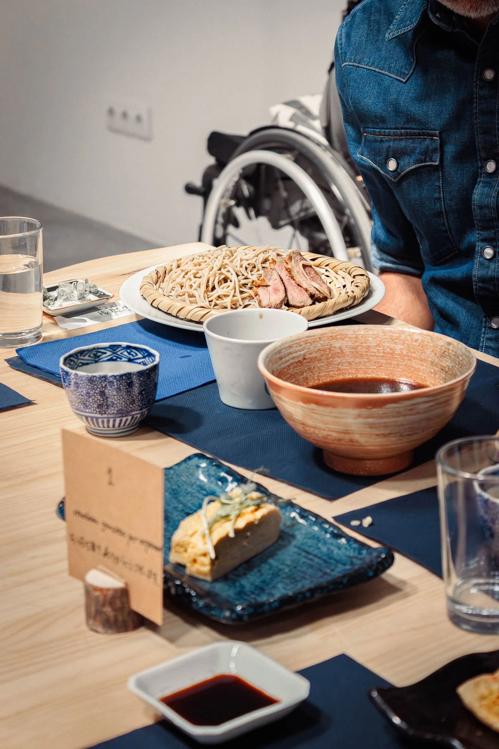 Table setting with soba noodles, dipping sauce, tea cup, and plated dessert at a Barcelona restaurant