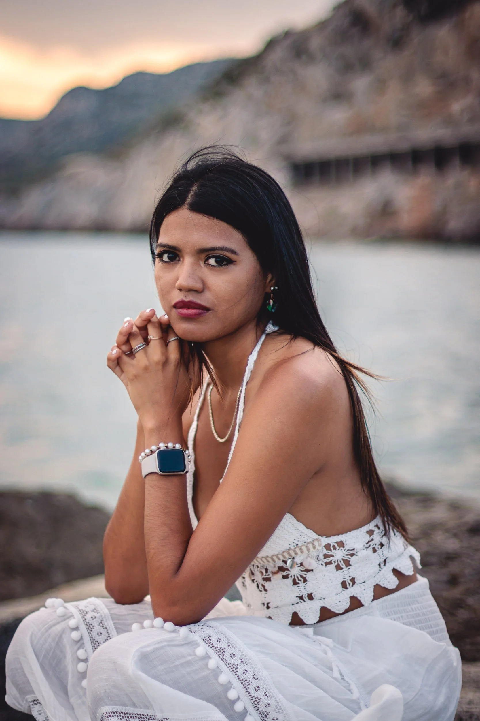 Close portrait of a woman seated on the beach in a white dress at sunset