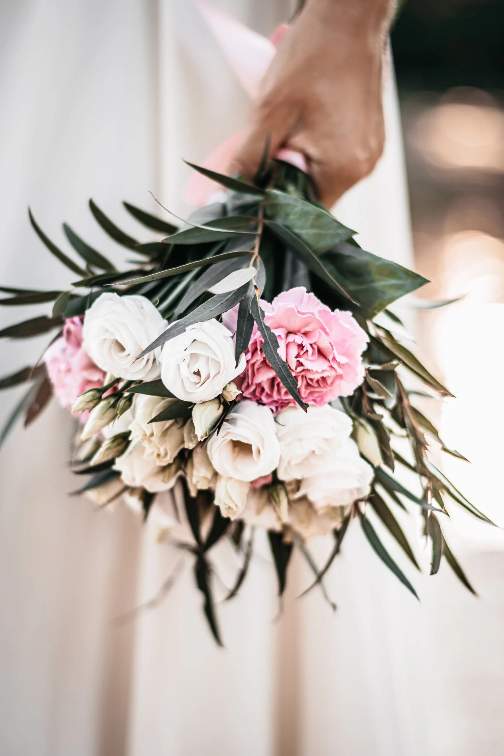 Close-up of the bride holding a pastel wedding bouquet beside her dress