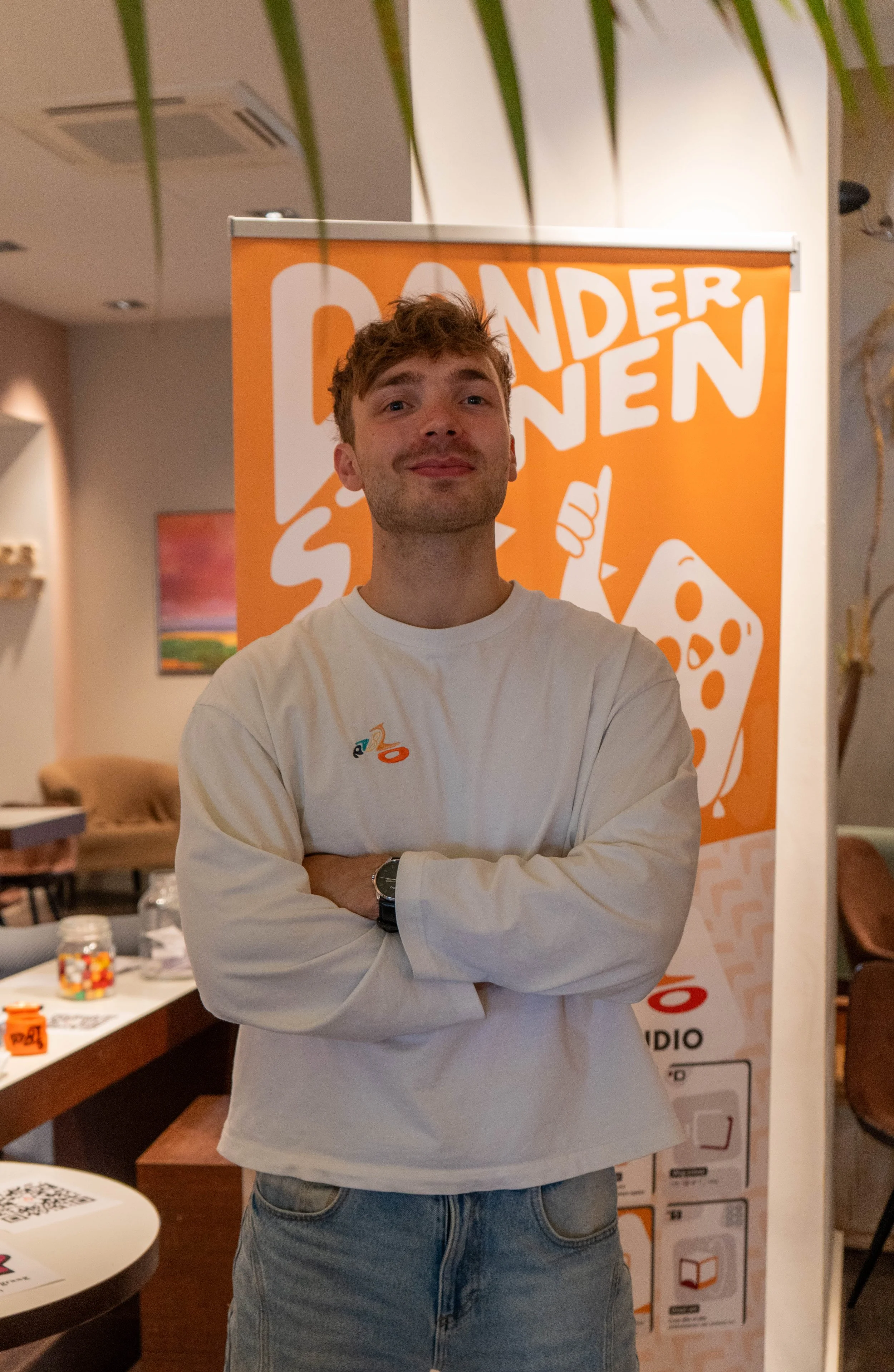 Tycho van den Bosch, eigenaar StudioPablo, met een witte lange mouwen t-shirt met het scooter logo van StudioPablo. Achter hem de donderstenen banner.