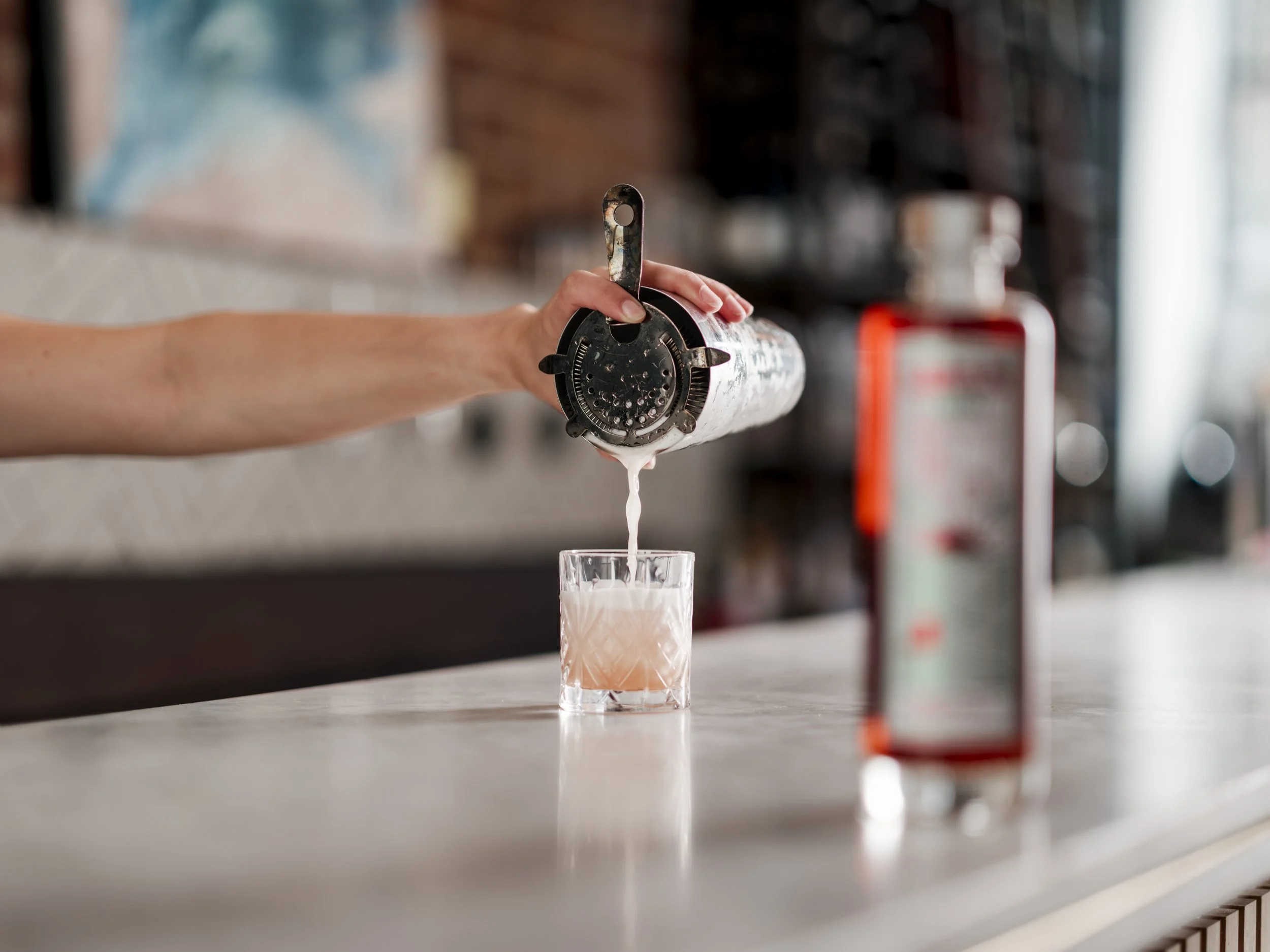 A person pouring a cocktail from a shaker into a glass.