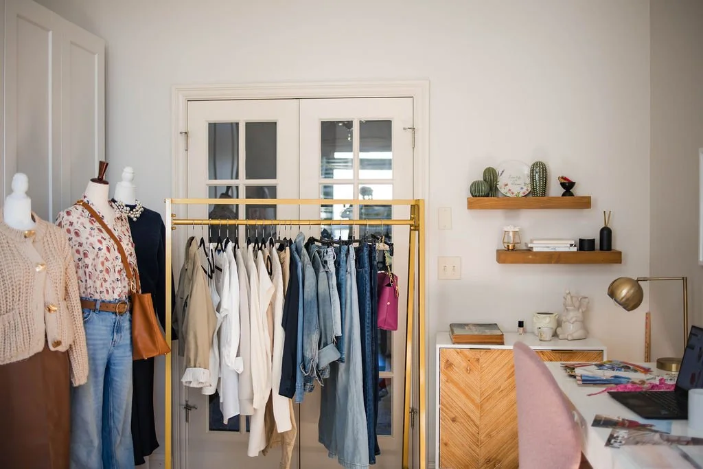 Room with clothing rack, mannequins, and desk with laptop and decor.