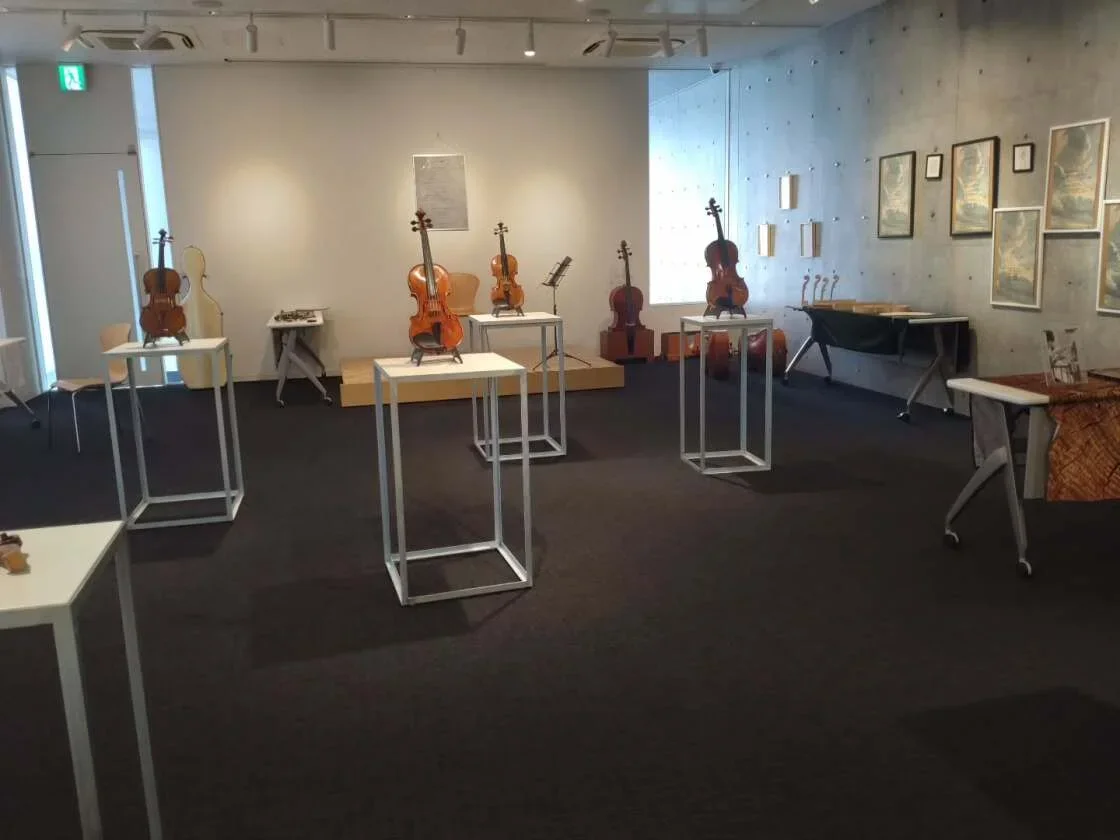 室内の展示スペースにバイオリンがいくつか置かれている。壁にはいくつかの絵画が飾られ、木製の椅子やテーブルも見える。